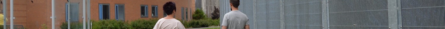 Eine Mitarbeiterin aus dem Pflege- und Erziehungsdienst geht mit einem Patienten an dem 5,50 hohen Sicherheitszaun entlang.